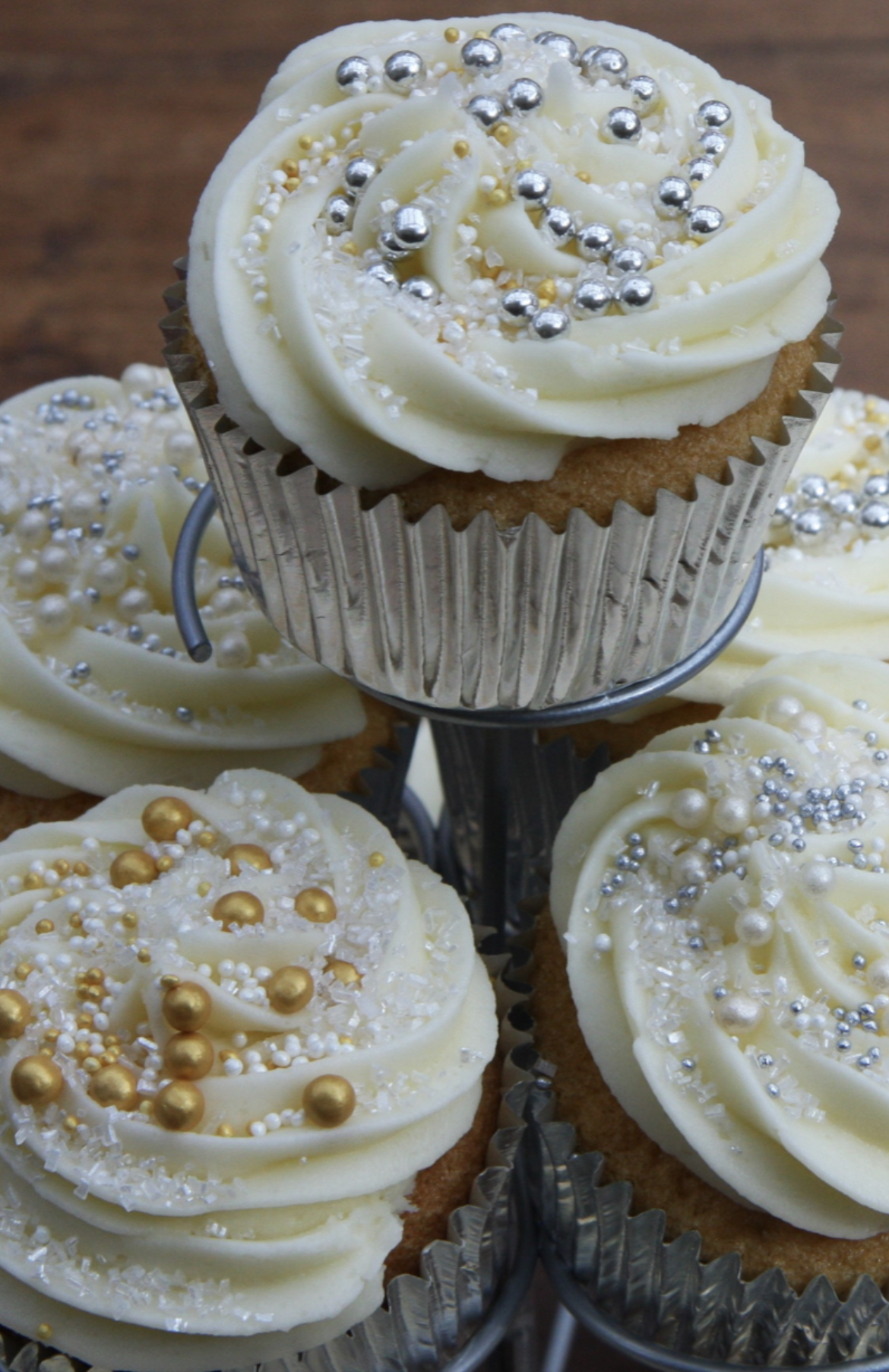 Picture depicts gold and silver edible decorations on top of sponge cupcake, topped with buttercream of cream cheese frosting. Silver foil cupcakes.