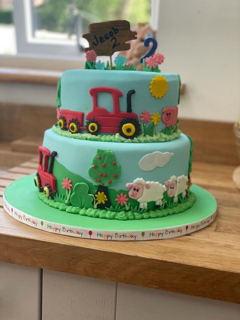 Picture depicts two tier sponge cake with choice of filling, ganache crumb coat and fondant decorations depicting farm theme.